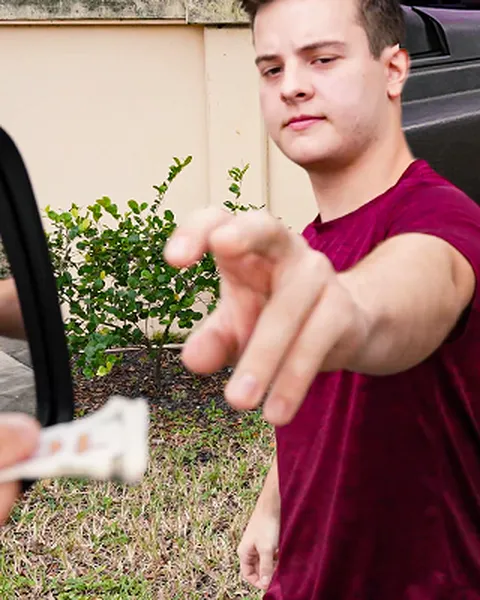 Promotional still from Gay Wire showing a man in a maroon T-shirt outdoors beside a car