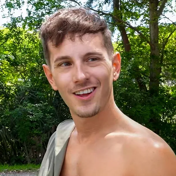Gay Wire model Ralph Seven smiling shirtless outdoors with a T-shirt slung over his shoulder