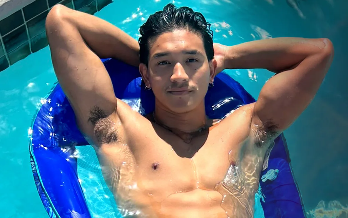 PeterFever model Andrew Akito, shirtless and wet in flamingo swim trunks, lounging on a pool float with his arms behind his head