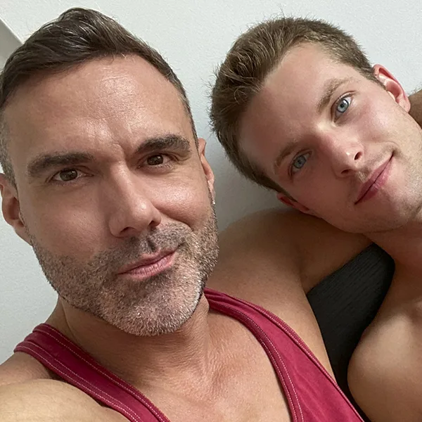 Say Uncle: two men in bed taking a selfie, one shirtless with blue eyes and one in a red tank top